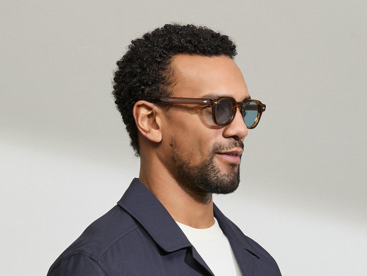 Model is wearing The DOLT SUN in size 46 in Cognac with Mineral Blue Tinted Lenses