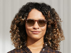 Model is wearing The MAYDELA CLIP in Gold in size 49 with Forest Wood Tinted Lenses