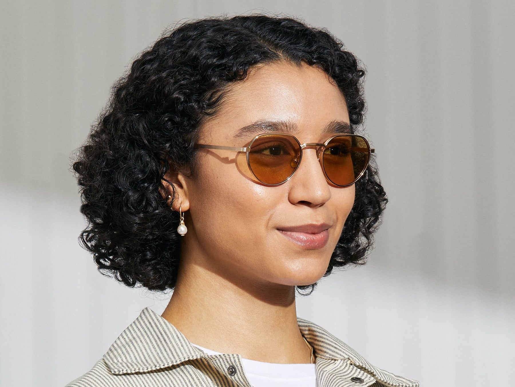 Model is wearing The SMENDRIK SUN in Gold in size 51 with Amber Tinted Lenses